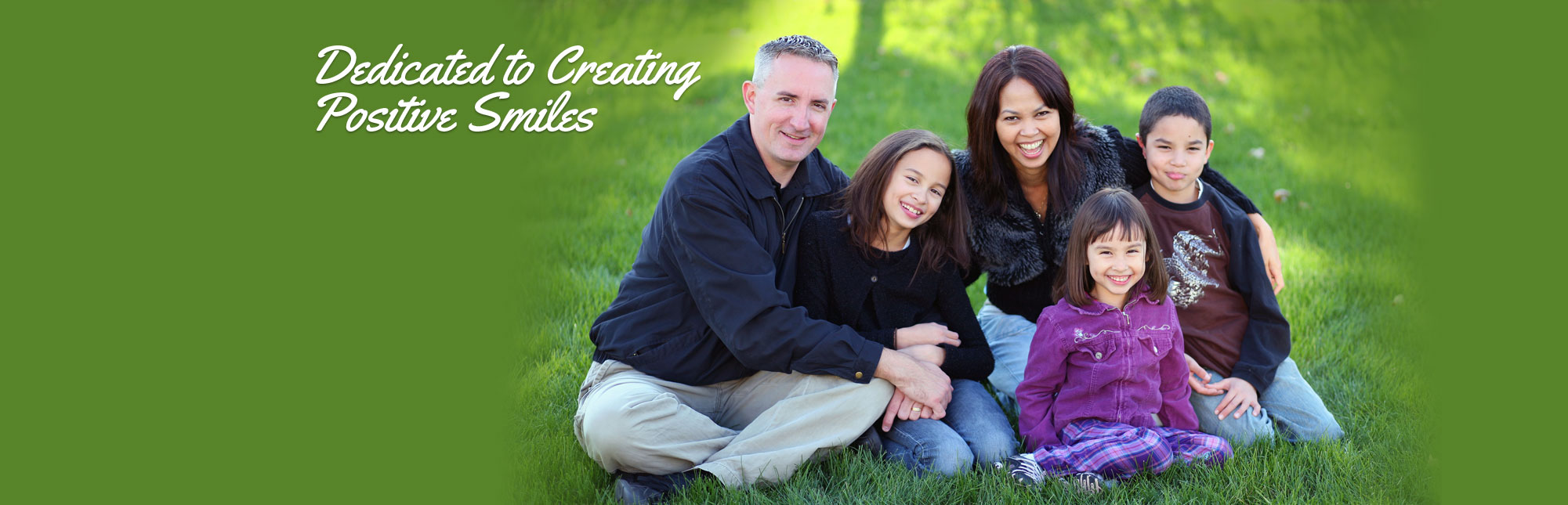 Similing family with young children sitting in the grass - Dedicated to Creating Positive Smiles